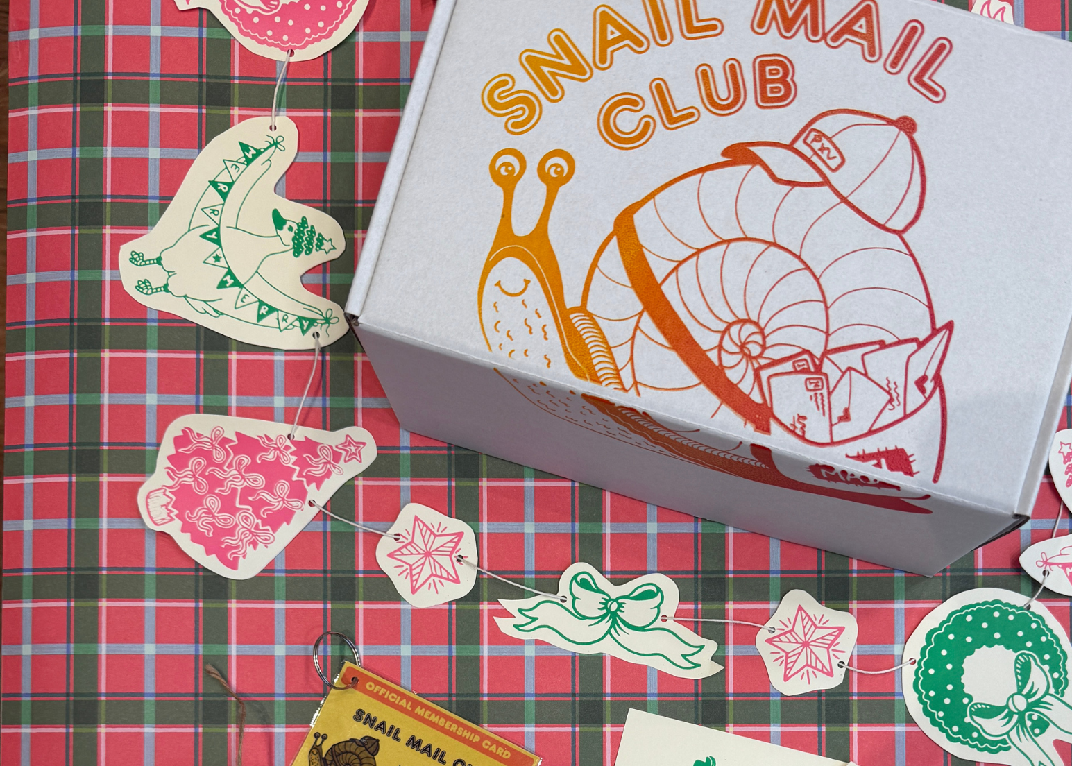 Snail Mail Club packaging with stickers and cards on a red plaid background